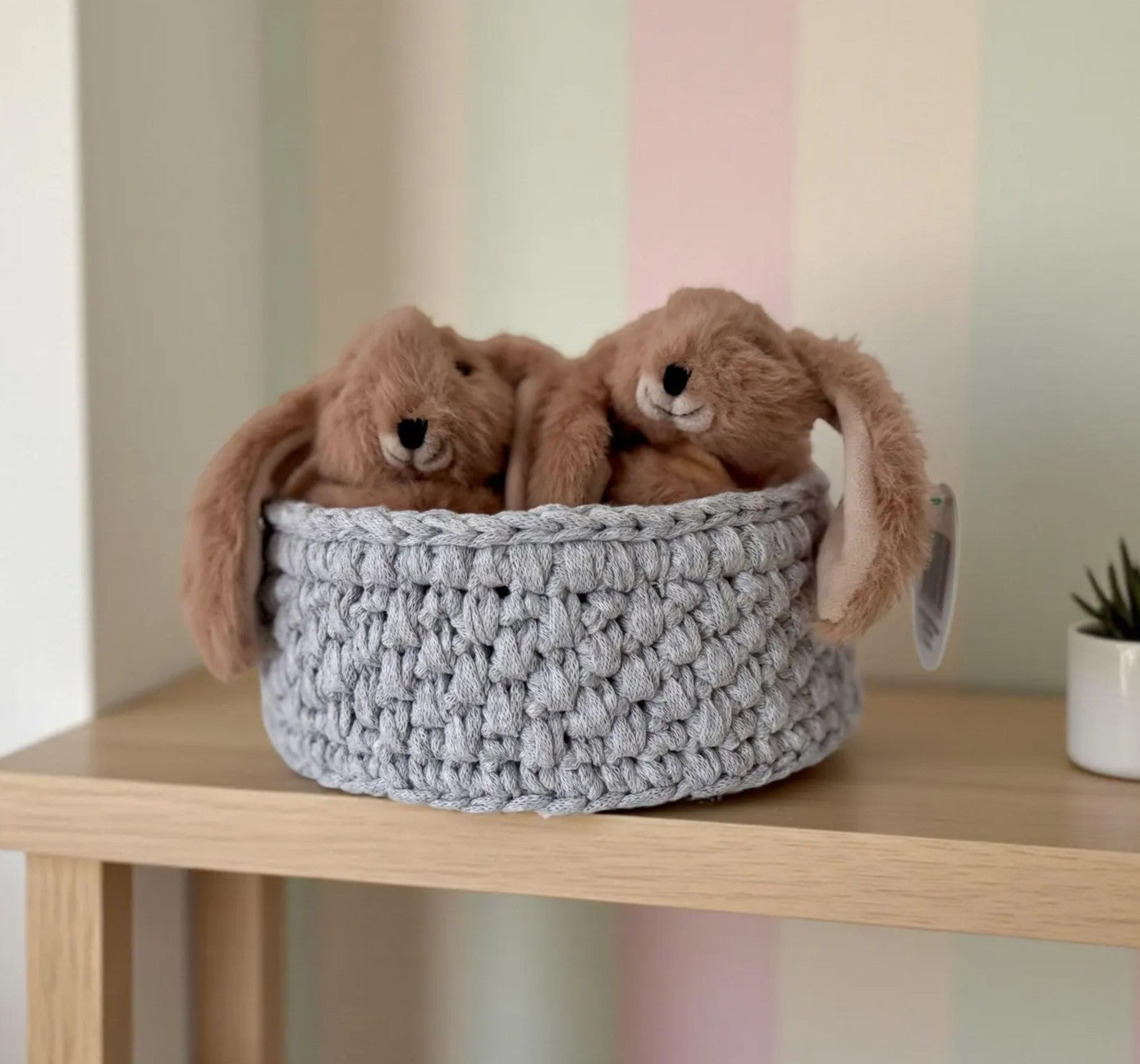 Handmade crochet storage basket filled with soft toy rabbit slippers, a thoughtful affordable gift for a nursery or child's bedroom.