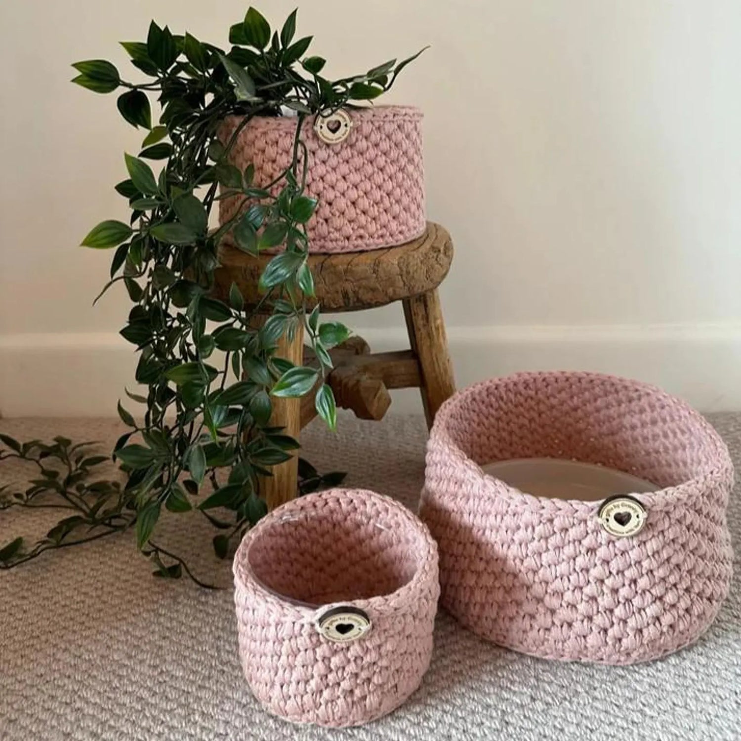 Handmade pink crochet storage baskets in three sizes styled in a living room with a houseplant, made from recycled cotton yarn.