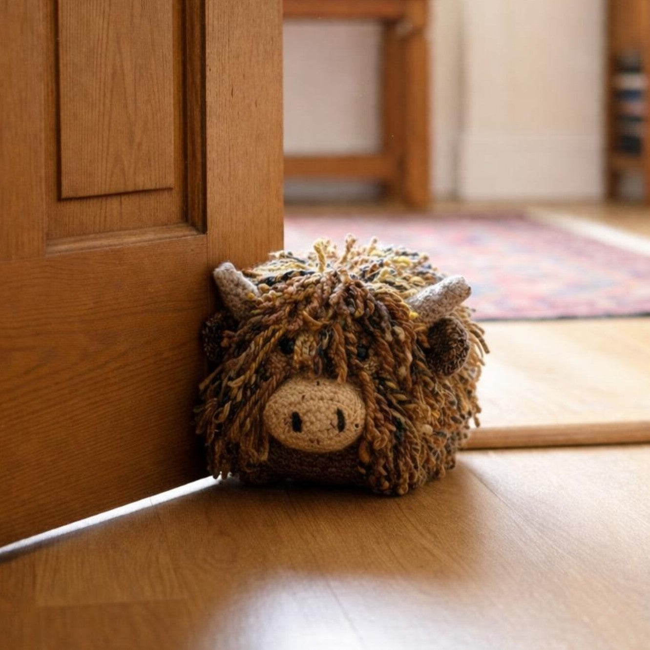 Handmade Highland cow crochet doorstop sitting by a wooden door, adding character and charm to a cosy home.