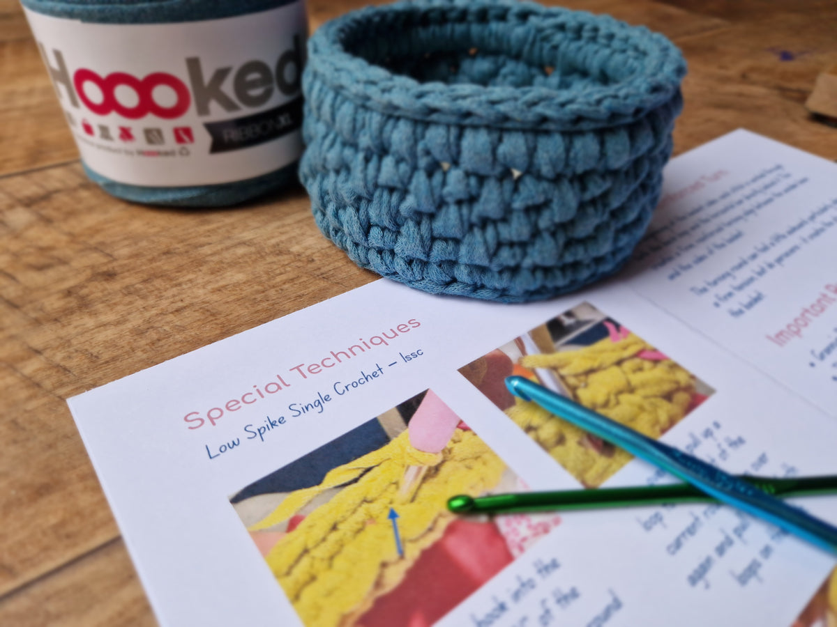 Handmade blue crochet trinket basket beside illustrated crochet pattern instructions