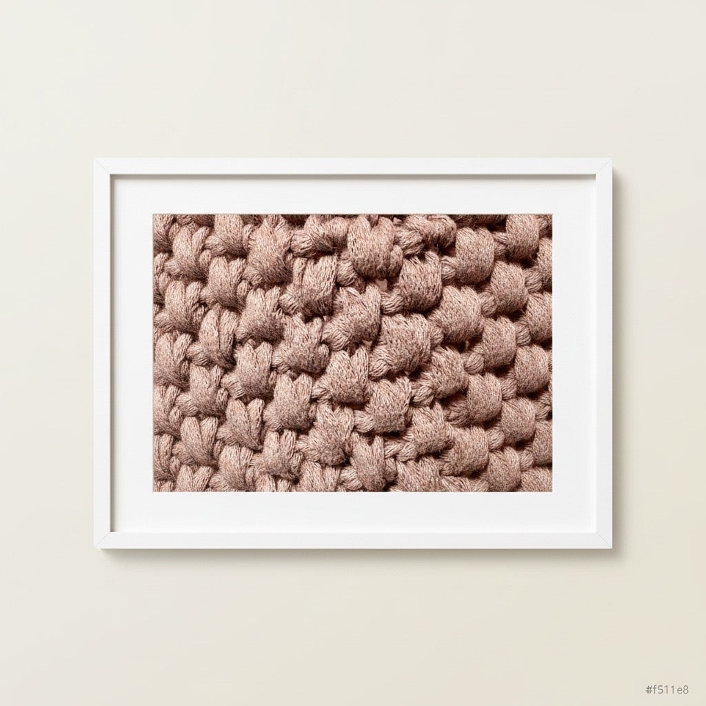 A framed art print showcasing a close-up of crochet stitches of a handmade storage pot in colour Ecru, set in a clean white frame against a neutral light beige wall.